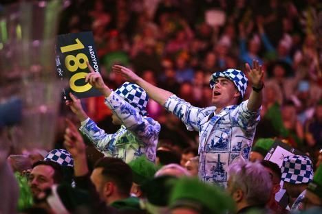 Darts fans cheering, holding up a 180 score sign.