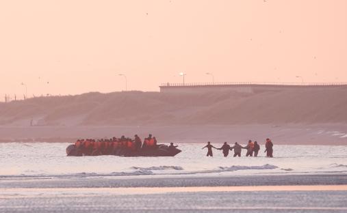 Migrants in a small boat leaving a beach.