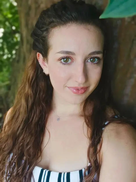 A young woman with long wavy brown hair, hazel eyes, and light skin looks at the camera.