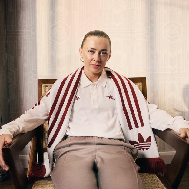 A woman sits in a chair wearing an Arsenal third kit.