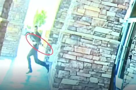 Surveillance footage of a man carrying a rifle running inside a building.