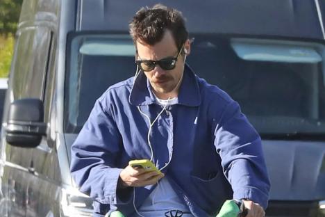 Pop star Harry Styles looks down at phone while riding electric bike without helmet on busy London road