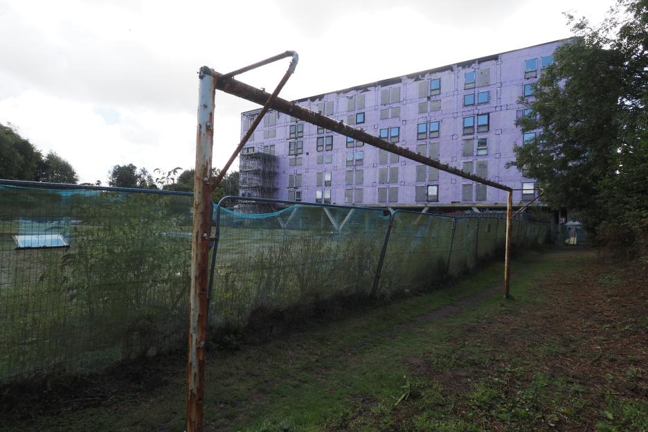 Derelict purple student accommodation block in Penryn, Cornwall, with boarded-up windows and overgrown grounds behind a fence.