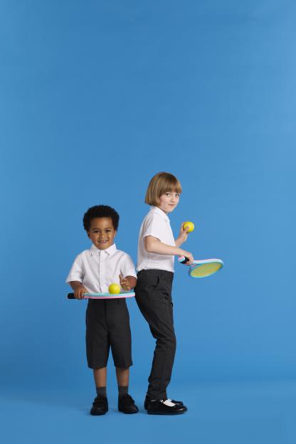 Two children in school uniforms playing tennis.