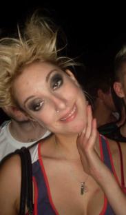 Woman with blonde hair and dark eye makeup smiling.