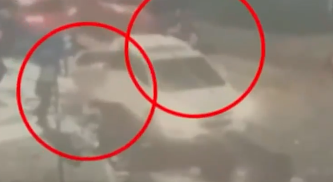 Blurry image of a car with two red circles highlighting a figure standing next to the car.
