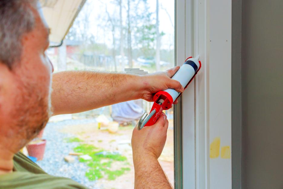 Homeowner applying caulk around a window frame for insulation.