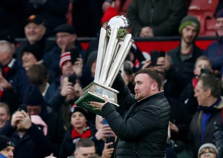 A man holding the 2025 PDC World Darts Championship trophy aloft in front of a crowd.