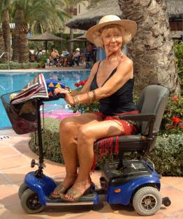 Sheila Reid as Madge on a mobility scooter by a pool.