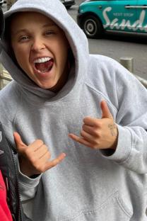 Woman in gray hoodie making shaka sign.