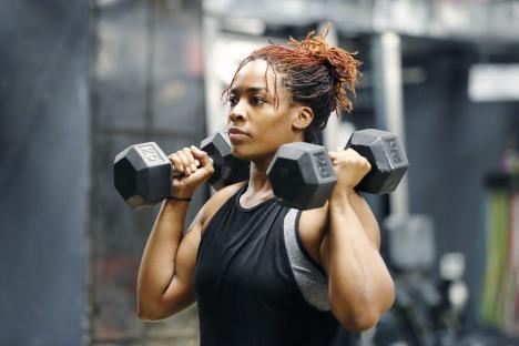 A young African American woman lifting weights at the gym.