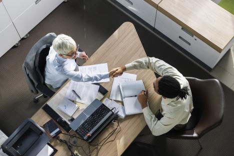High-angle view of a job interview: a man and woman shaking hands across a desk.