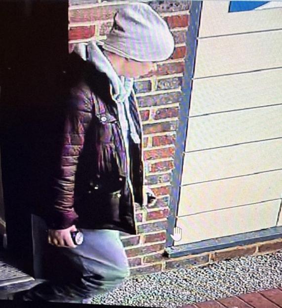 Surveillance photo of Amelia Murton, wearing a grey hooded top, a burgundy coat, light-colored trousers, and a white beanie hat.