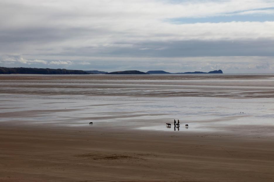 View across Carmarthen Bay with people walking dogs on the beach.