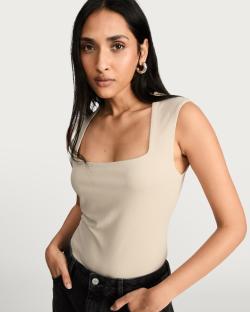 Woman wearing a beige square-neck sleeveless top and dark jeans.