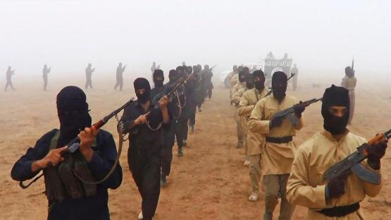 ISIS fighters marching with firearms in foggy conditions.