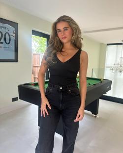 Woman in black top and jeans standing near a pool table.
