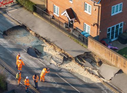 Workers inspecting a large sinkhole in a road.