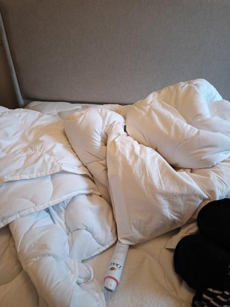 Unmade bed with white duvet and sheets, a Dove deodorant stick, and a pair of black slippers.