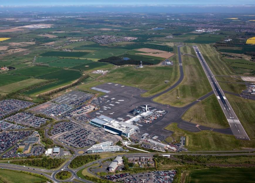 Aerial view of Newcastle Airport, showing runways, terminals, parked aircraft, and surrounding parking lots and fields.