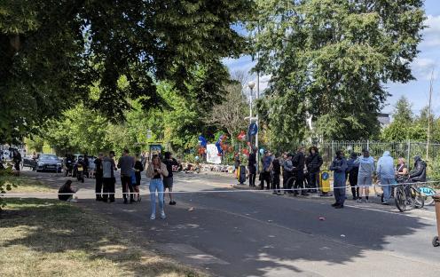 People gathered at a roadside memorial with balloons and flowers.