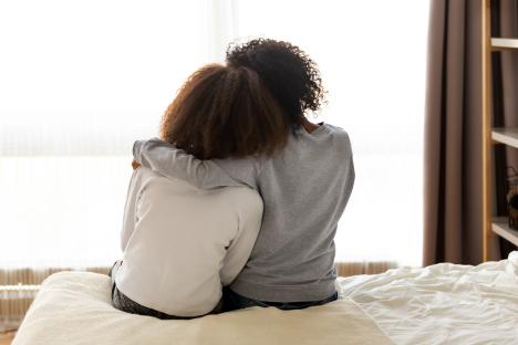 Rear view of a mother and daughter embracing on a bed.