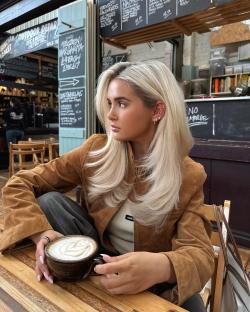 Woman with blonde hair sitting at a cafe table holding a latte.