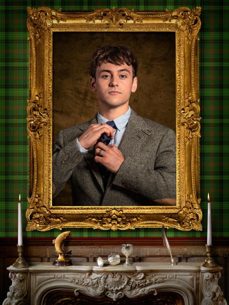 Tom Daley in a tweed jacket adjusting his tie, framed in an ornate gold picture frame.