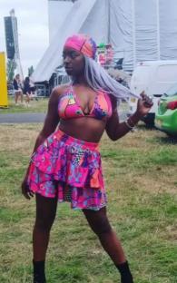 Woman in a pink and purple patterned bikini and skirt at an outdoor festival.