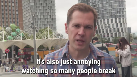 Man speaking to camera in city setting, text overlay reads: