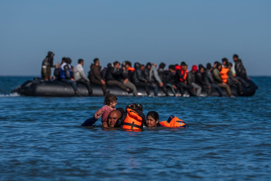 Migrant family in the water, approaching a boat full of other migrants.