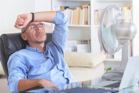 Man sweating at his desk in front of a fan.