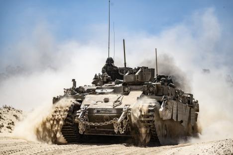 Israeli army tank moving along the border, kicking up dust.