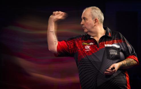 Phil Taylor throwing a dart during a darts match.