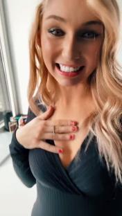 Woman smiling and adjusting her dark v-neck dress.