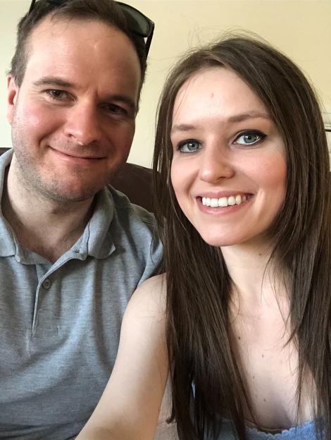 A man in a grey polo shirt and a woman with long brown hair smiling at the camera.