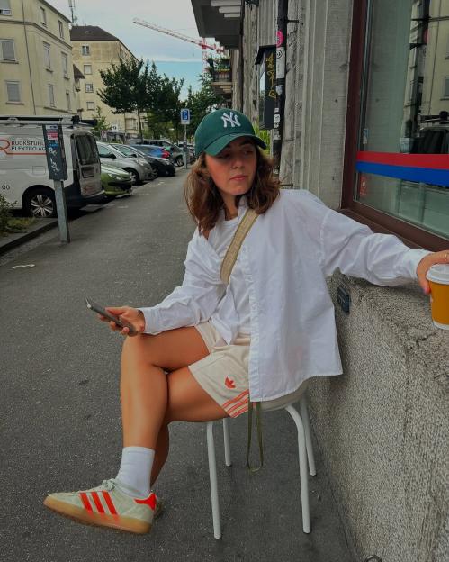 Woman sitting on a stool outdoors, holding a phone and coffee cup.