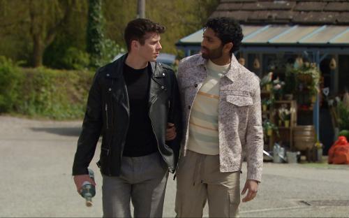 Two men walking and talking, one carrying a bottle.
