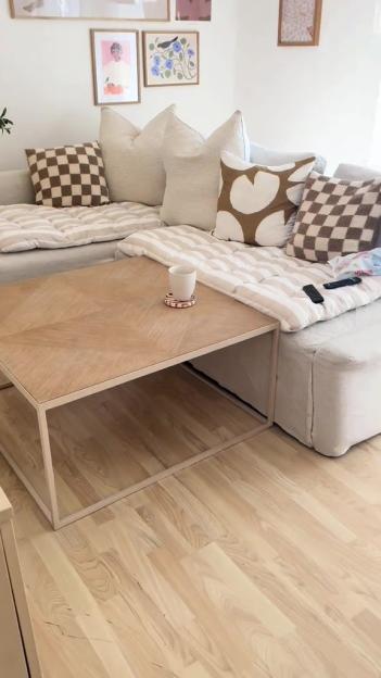 Living room with light wood flooring, a light beige sectional sofa with patterned pillows, and a light wood coffee table.