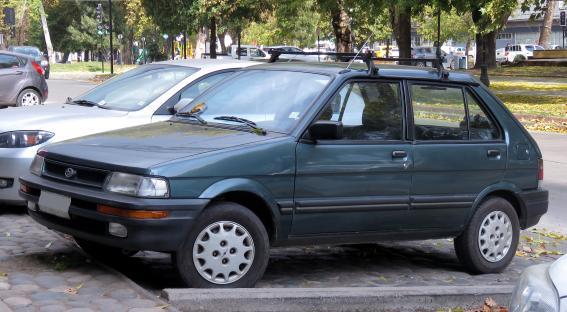 A dark-green Subaru Justy hatchback parked on a cobblestone street.