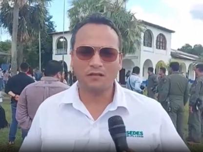 Man in sunglasses being interviewed with uniformed people in the background.