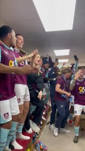 Burnley football players celebrating promotion with a singer in the locker room.