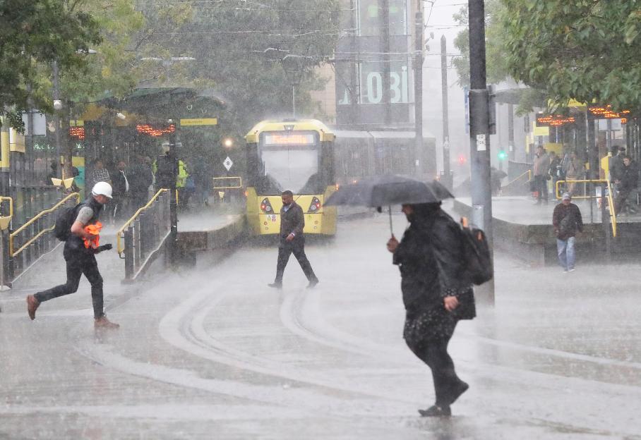 People navigating a rain-soaked city street near a tram.
