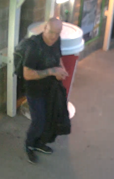 Surveillance image of a man with tattoos holding a dark garment.
