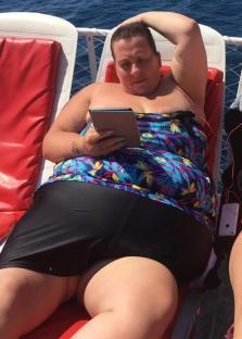 Woman in swimsuit reading a tablet on a boat.