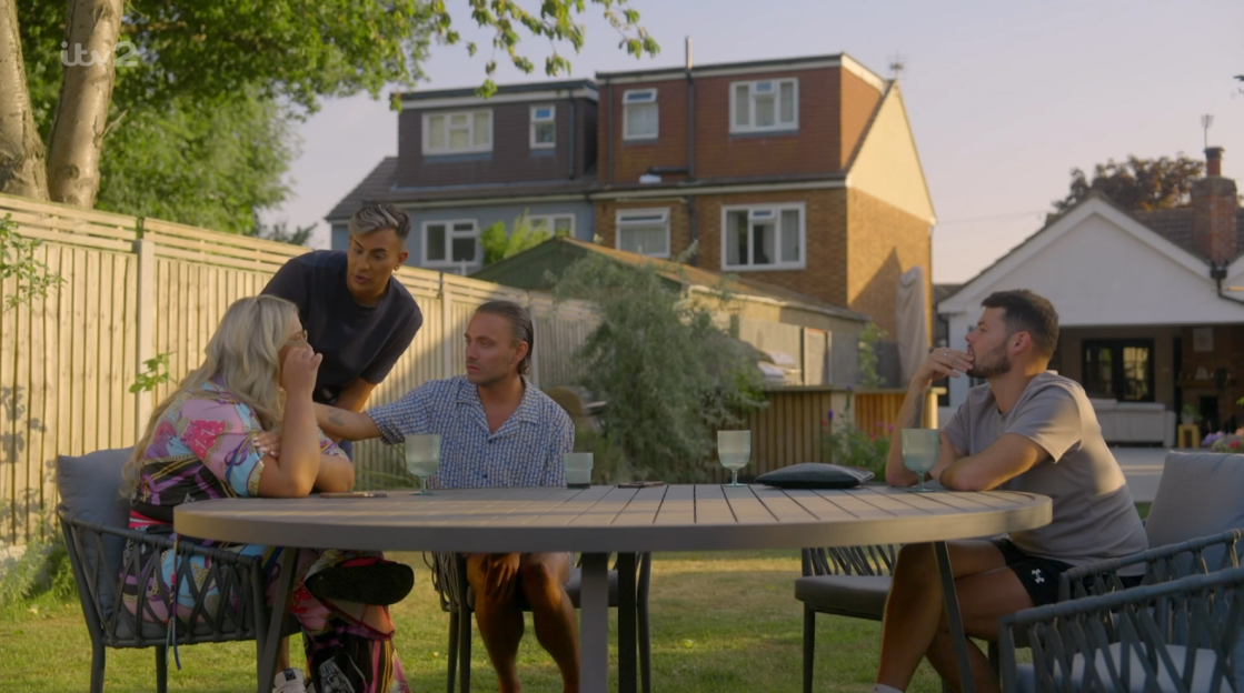 Screenshot of four people sitting at an outdoor table, one appearing upset.
