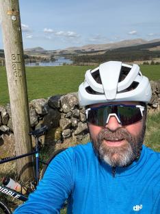 Man in cycling gear taking a selfie with his bike and a scenic view in the background.