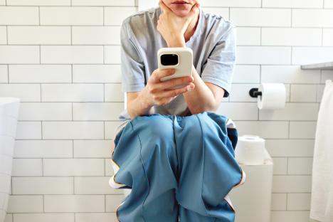 Woman using smartphone while sitting on toilet.