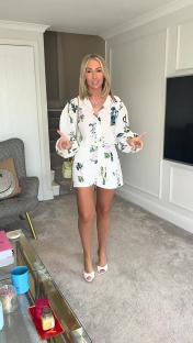 Woman in floral shirt and shorts standing in a living room.