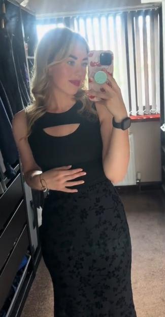Woman taking a mirror selfie in a black dress.